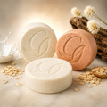Three goats milk and oatmeal lotin bars with pictures of milk, oud wood, and oats next to the cleansing bars.
