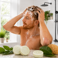 Man washing his hair with soap and water in a bathroom setting.